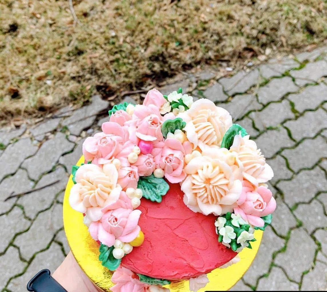 A hand holding a pink cake topped with pale pink buttercream flowers