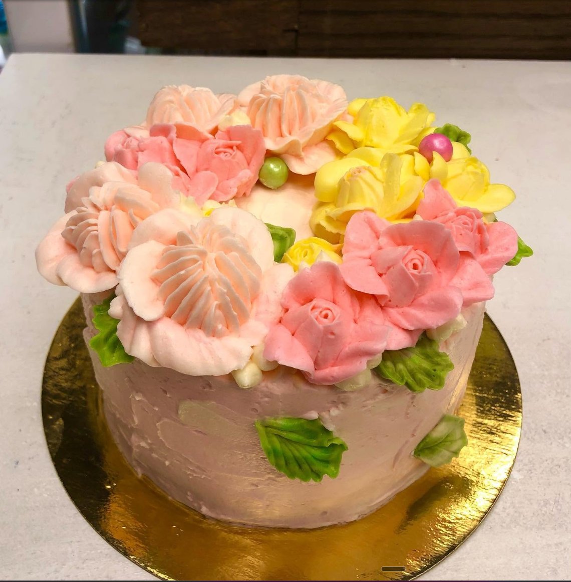 Pink cake with peach and yellow flowers on a gold board