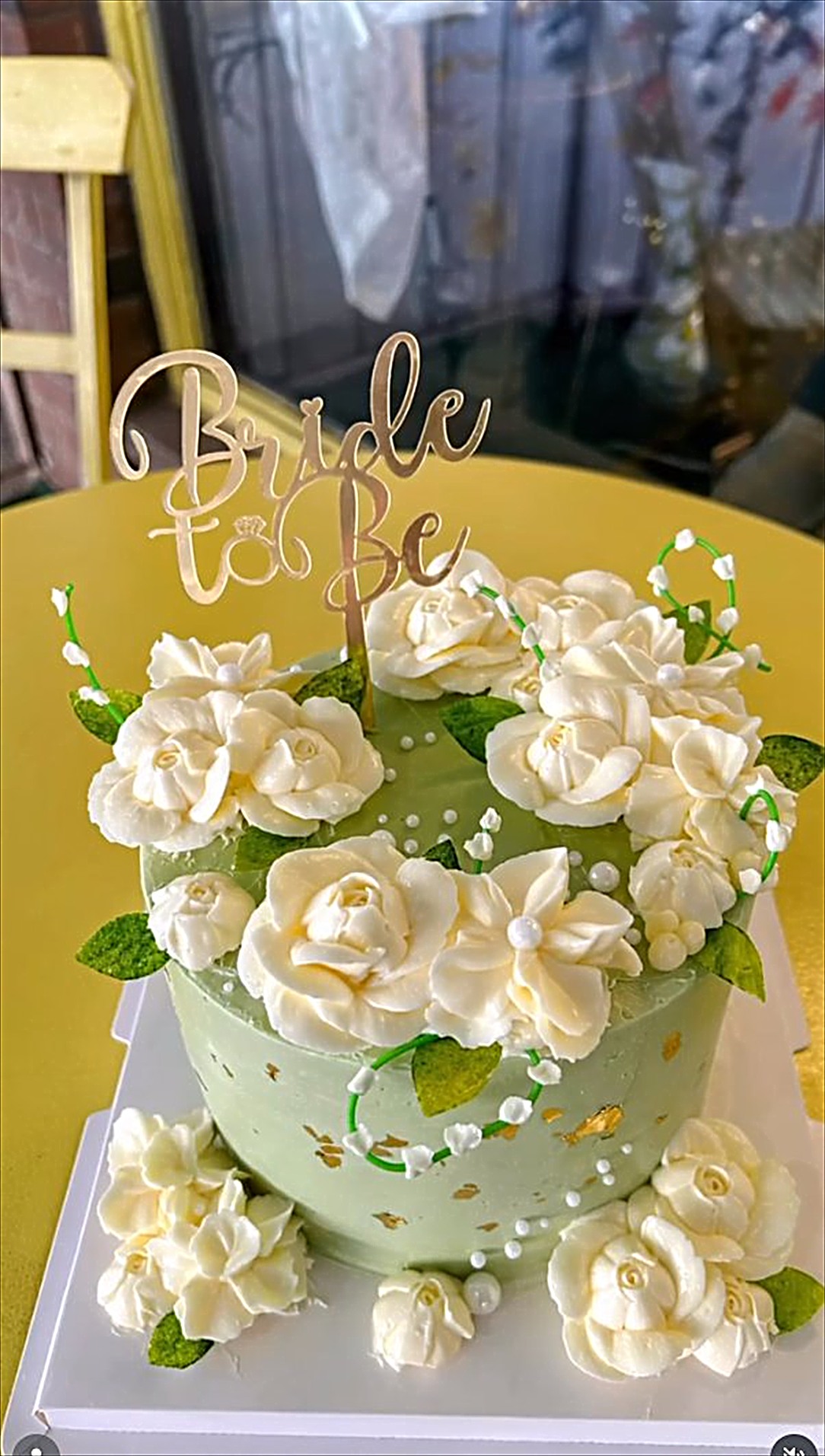 A pale green cake with white buttercream flowers and a Bride to Be topper