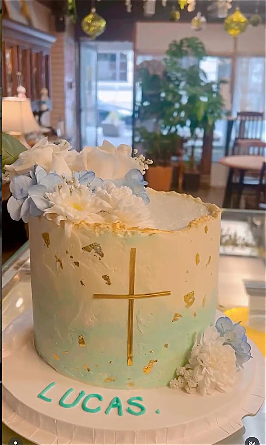 A pale blue tall cake with a gold cross and hydrangea for a communion