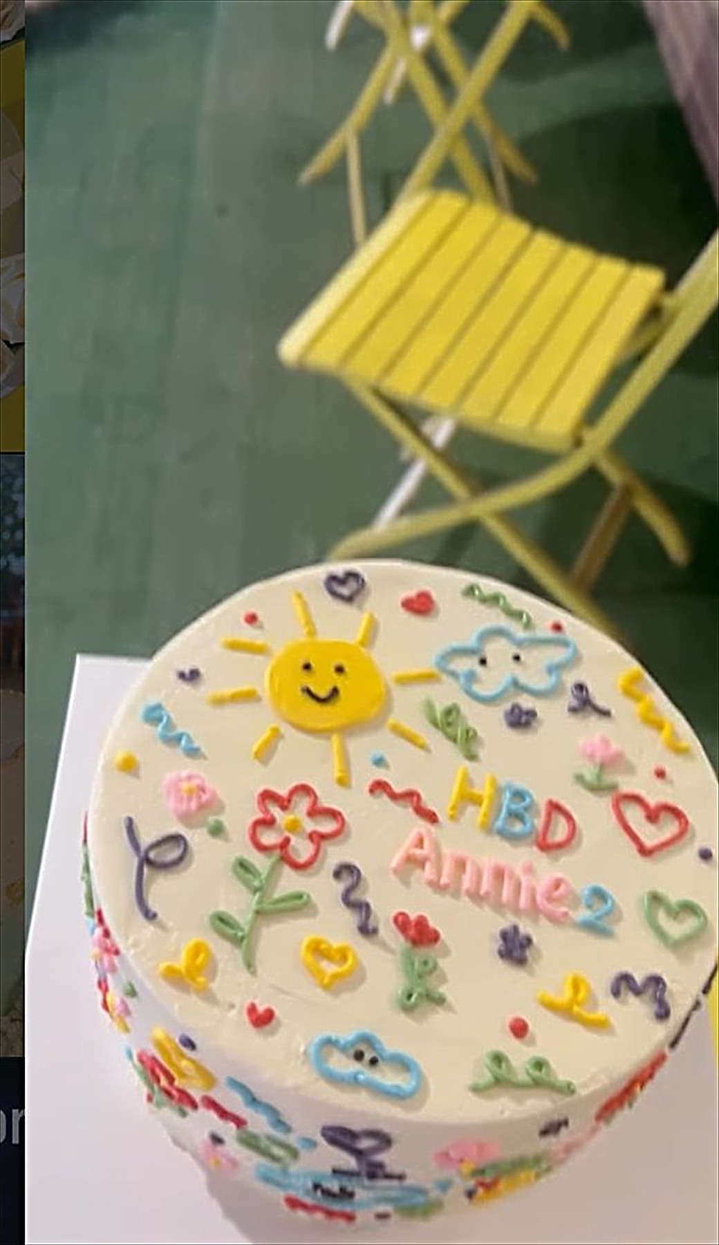 A white cake decorated with a colourful hand drawn design for a second birthday