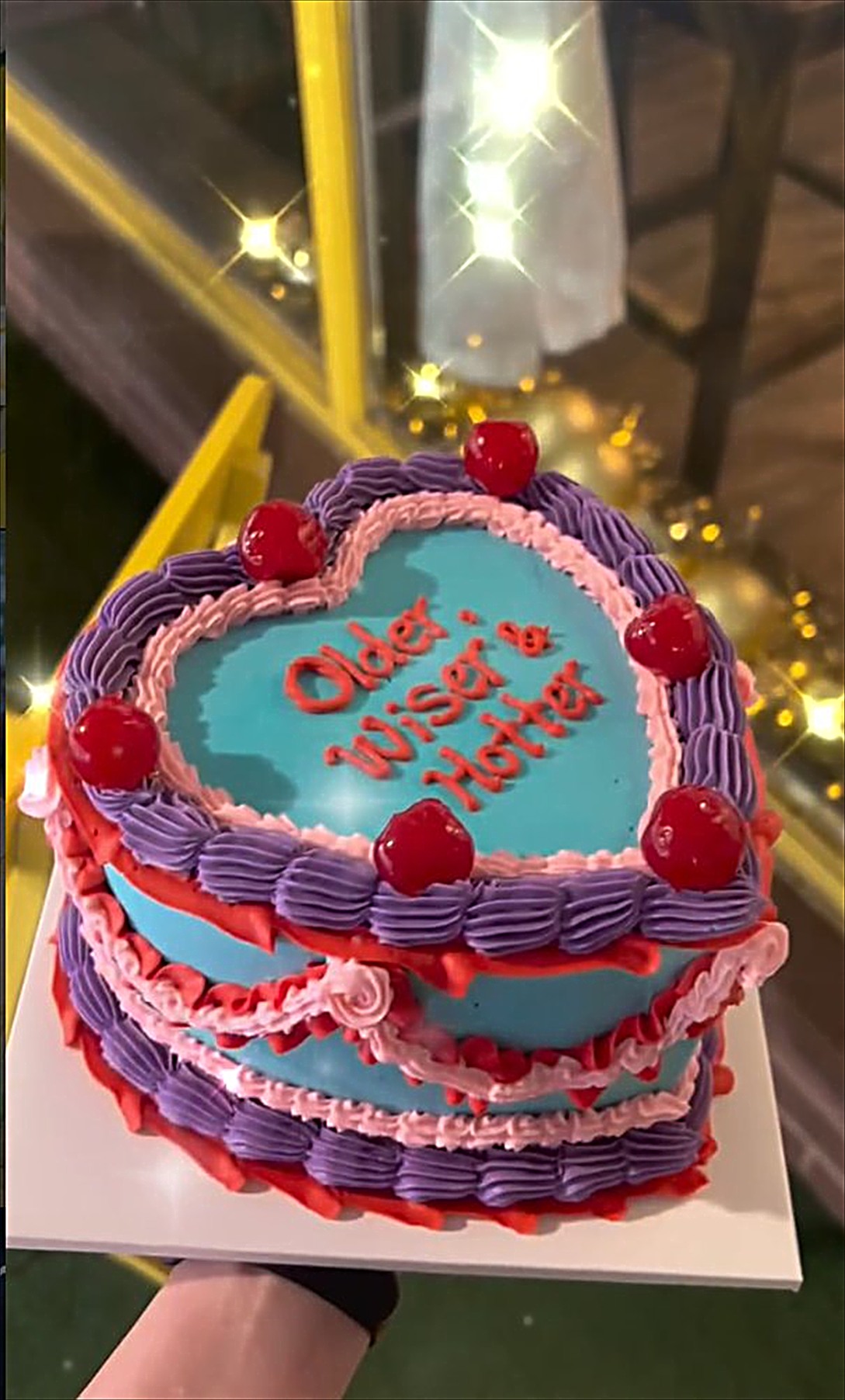 A blue heart shaped vintage cake with pink and purple piping and cherries