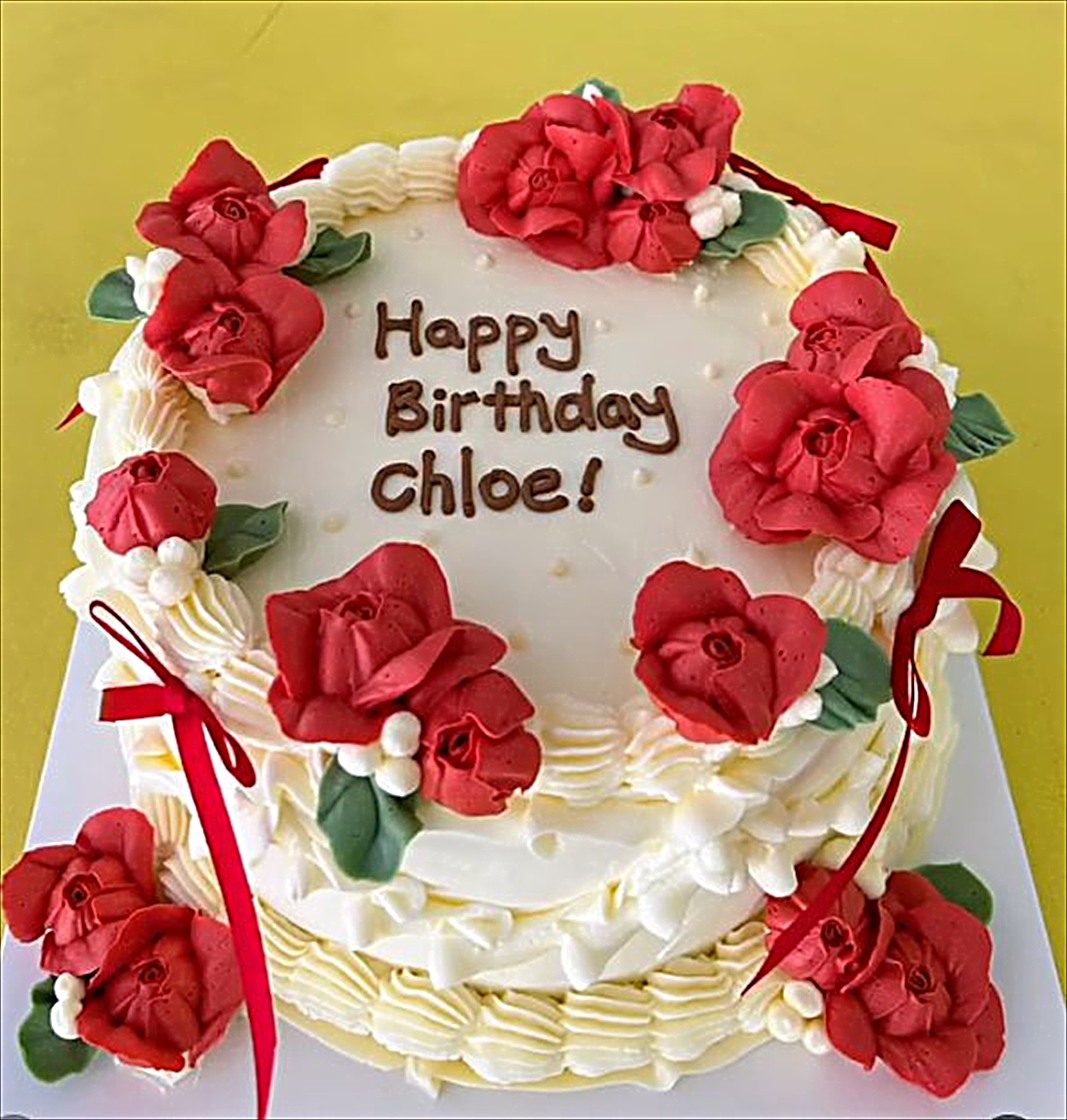 White cake with red roses and ribbons reading Happy Birthday Chloe