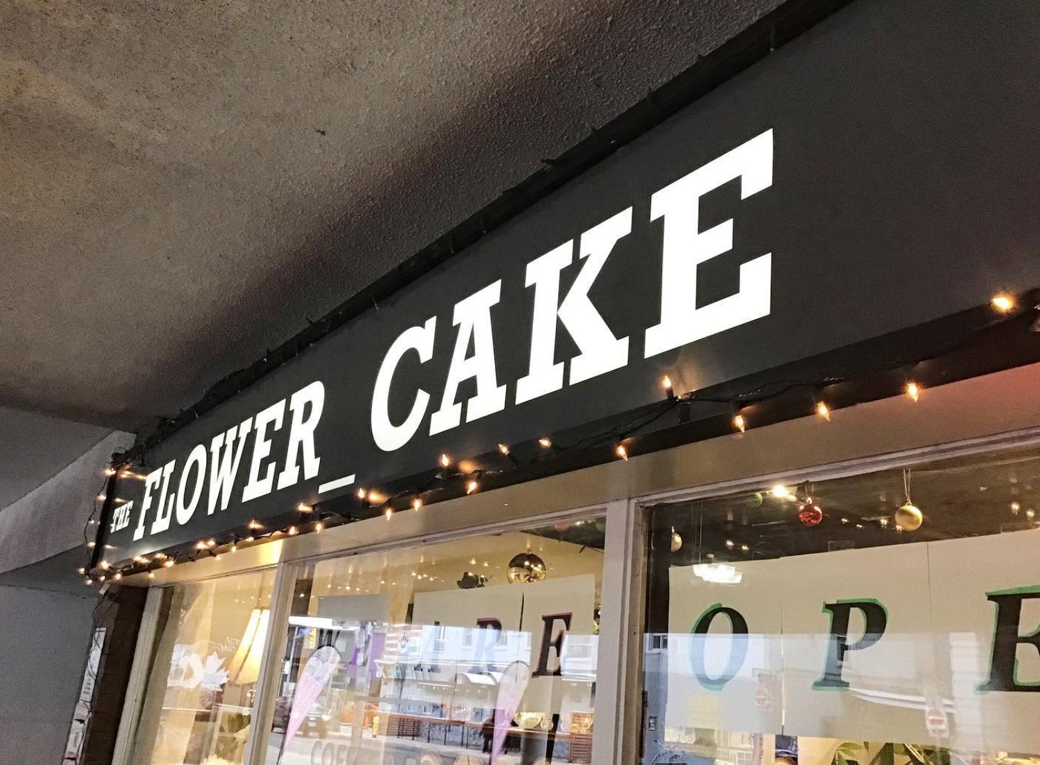 The Flower Cake storefront sign lit with string lights